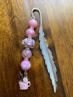 a pink beaded keychain with a feather charm attached to it on a wooden table