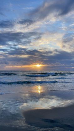 the sun is setting over the ocean with clouds reflected in the wet sand and water