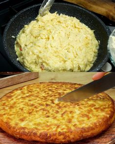 someone is cutting into a cheese pizza on a wooden board with a skillet in the background