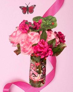 a vase filled with pink flowers sitting on top of a table next to a pink ribbon