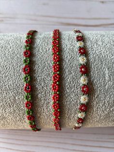 three red and green beaded bracelets sitting on top of a white cloth roll