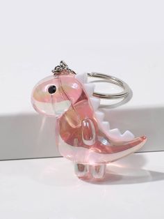 a pink dinosaur keychain sitting on top of a white table next to a wall