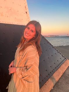 a woman standing in front of a metal structure near the ocean at sunset or sunrise