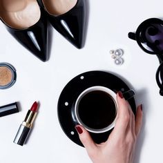 a woman's hand holding a cup of coffee next to some lipstick and eyeliners