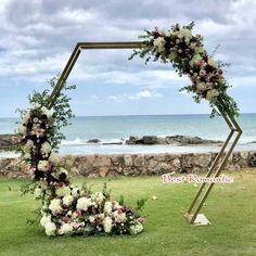 a wedding arch with flowers and greenery on the grass near the water's edge