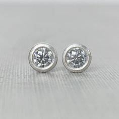 3 mm page grey moissanite stud earrings, bezel set in your choice of sterling silver or 14k gold. Choose from yellow, rose or white gold. May be ordered singly or in pairs. Sterling silver is pictured in the first three photos followed by 14k yellow gold and 14k white gold. These earrings are made to order and will ship within 3-5 days. They are TINY! (See photo in hand for scale.)DETAILS- 3 mm grey moissanite- bezel setting - satin finish- choice of solid 14k gold or sterling silver- clear plas Minimalist Silver Diamond Earrings With Single Diamond, Minimalist Sterling Silver Diamond Earrings For Anniversary, Minimalist Solitaire Sterling Silver Diamond Earrings, Minimalist Sterling Silver Solitaire Diamond Earrings, Silver Minimalist Diamond Earrings With Brilliant Cut, Minimalist Everyday Earrings With Bezel Setting, Everyday Minimalist Earrings With Bezel Setting, Anniversary Diamond Earrings With Tension Setting, Classic Sterling Silver Diamond Earrings