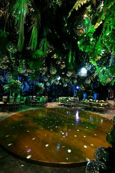 a large circular table surrounded by green chairs and lights in a room filled with plants