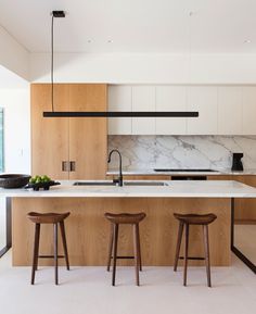 two stools sit in front of an island with marble countertops and wooden cabinets