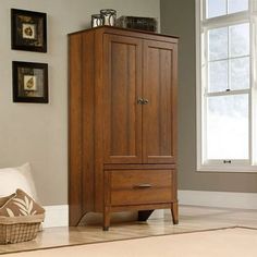 a tall wooden cabinet sitting next to a window in a room with white carpet and pictures on the wall