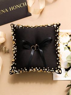 a black pillow with a ring on it next to some white flowers and a book