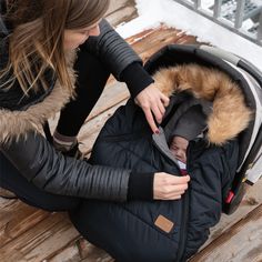 a woman sitting on a bench holding a baby in a stroller with the hood up