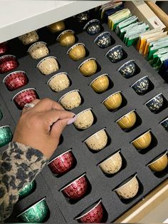 a person's hand is picking up some cups from a drawer full of them