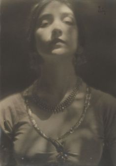 an old black and white photo of a woman with necklaces on her neck looking up