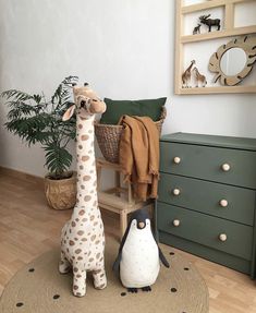 a stuffed giraffe next to a toy penguin on a rug in a child's room