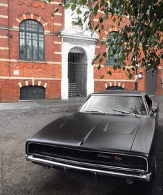 an old black muscle car parked in front of a brick building