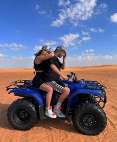 a man and woman riding on the back of a blue four - wheeler in the desert