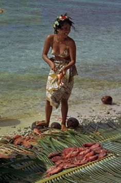 a woman standing on top of a sandy beach next to the ocean holding a knife