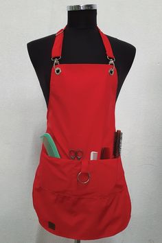 a red apron with scissors, combs and other items in it on a mannequin