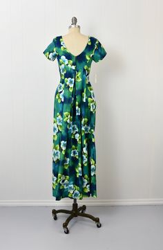 "Info: ♥ Circa: 60s ♥ Label: Ui-Maikai ♥ Color: Blue, green, white ♥ Material: Cotton ♥ Condition: Mint deadstock condition. Details: ♥ Amazing NOS 60s era Hawaiian dress by Ui-Maikai, complete with original tags! ♥ Cotton material in shades of blue, green, and white, featuring a hibiscus floral print ♥ Interior waist has two attached ties to create extra cinch ♥ Elegant fabric draping at back ♥ Unlined ♥ Back center zipper closure Measurements: Bust: 31\"-32\" Waist: 33\" (uncinched) Hips: 47\" Green Hawaiian Floral Print Dress, Green Hawaiian V-neck Dress, Retro Green Floral Print Maxi Dress, Green Tropical Print Short Sleeve Maxi Dress, Green Retro Maxi Dress With Floral Print, Green Tropical Print Maxi Dress With Short Sleeves, Green Maxi Dress With Tropical Print And Short Sleeves, Green Short Sleeve Maxi Dress With Tropical Print, Fitted Green Maxi Dress With Tropical Print