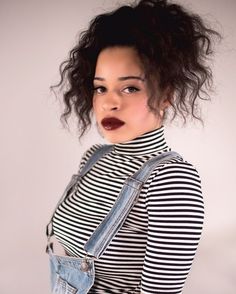 a woman with curly hair wearing a black and white striped shirt is posing for the camera