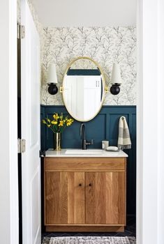 a bathroom with blue walls and wooden cabinetry, white sink and large round mirror