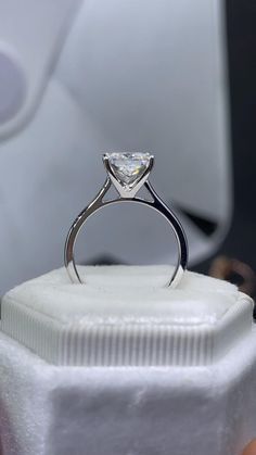 an engagement ring with a princess cut diamond on it's side sitting on top of a white box