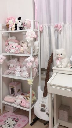 a room filled with lots of stuffed animals next to a white desk and guitar sitting on top of it