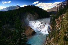 a large waterfall in the middle of a forest next to a river with blue water