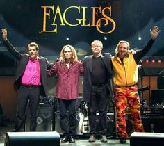 the eagles on stage with their arms in the air and one man holding his hands up