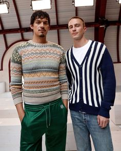 two men standing next to each other wearing sweaters