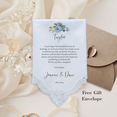 a wedding card with an envelope and ring on it, surrounded by white satin flowers