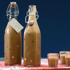 two glass bottles filled with liquid sitting on top of a red table cloth next to a cup