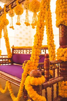 a bed covered in yellow flowers next to a purple pillow and wooden posts with chains hanging from it