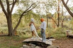 two people standing on top of a wooden platform in the woods with trees behind them