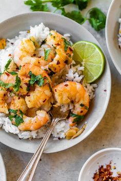 two bowls filled with shrimp and rice next to lime wedges, cilantro