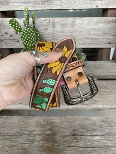 a person is holding up a flowered belt on a bench with cactus in the background