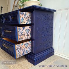 a blue dresser with floral designs painted on it's sides and drawers, next to a potted plant