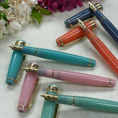 four different colored pens sitting next to each other on top of a white table with flowers in the background