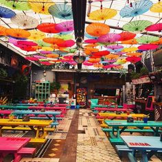 many colorful umbrellas are hanging from the ceiling in a restaurant with tables and benches