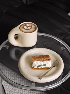 a glass table topped with a piece of cake and a cup of cappuccino