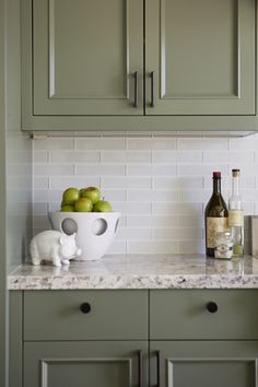 a white bowl filled with apples sitting on top of a counter next to green cabinets