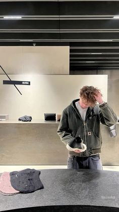 a man standing in front of a counter talking on a cell phone while wearing a jacket