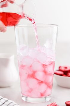 someone pouring red liquid into a glass filled with ice