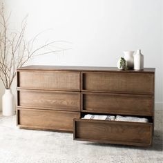 a large wooden dresser with drawers and vases on it's top shelf, in front of a white wall