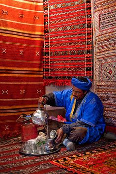 a man sitting on the ground in front of some rugs and making something out of paper