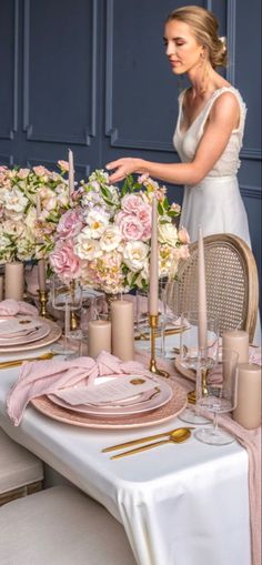 a woman setting a table with pink and white flowers