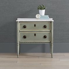 a white table with two drawers and a potted plant on top, against a gray wall