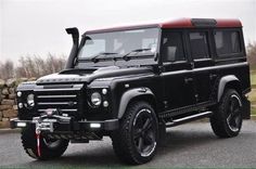 a black and red land rover is parked in the parking lot next to a stone wall