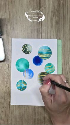 a person is painting some blue and gold ornaments on paper with watercolor pencils