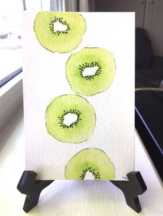 a card with three green apples on it sitting on a table next to a window